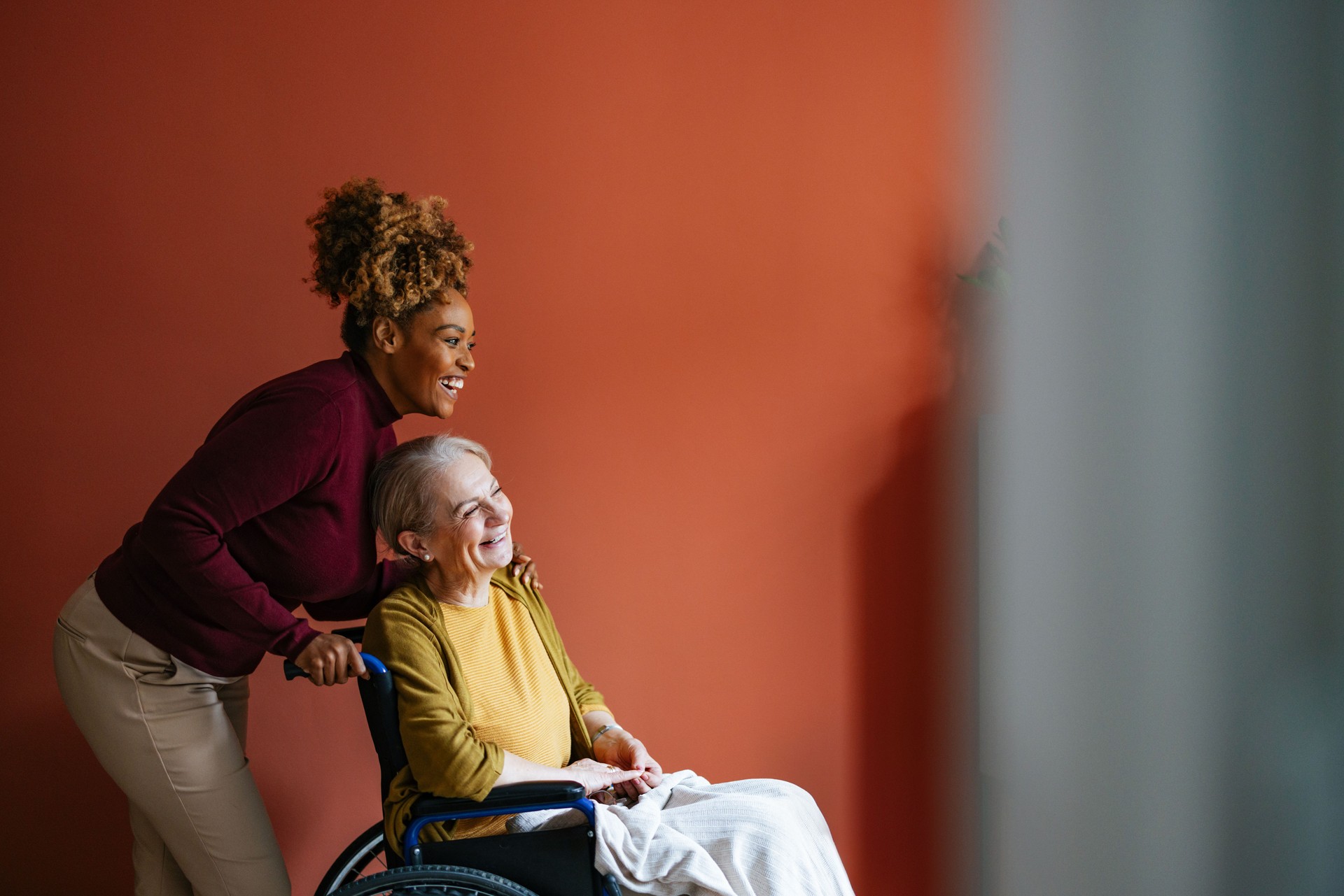Cheerful Caregiver Assisting Senior Woman in Wheelchair Indoors